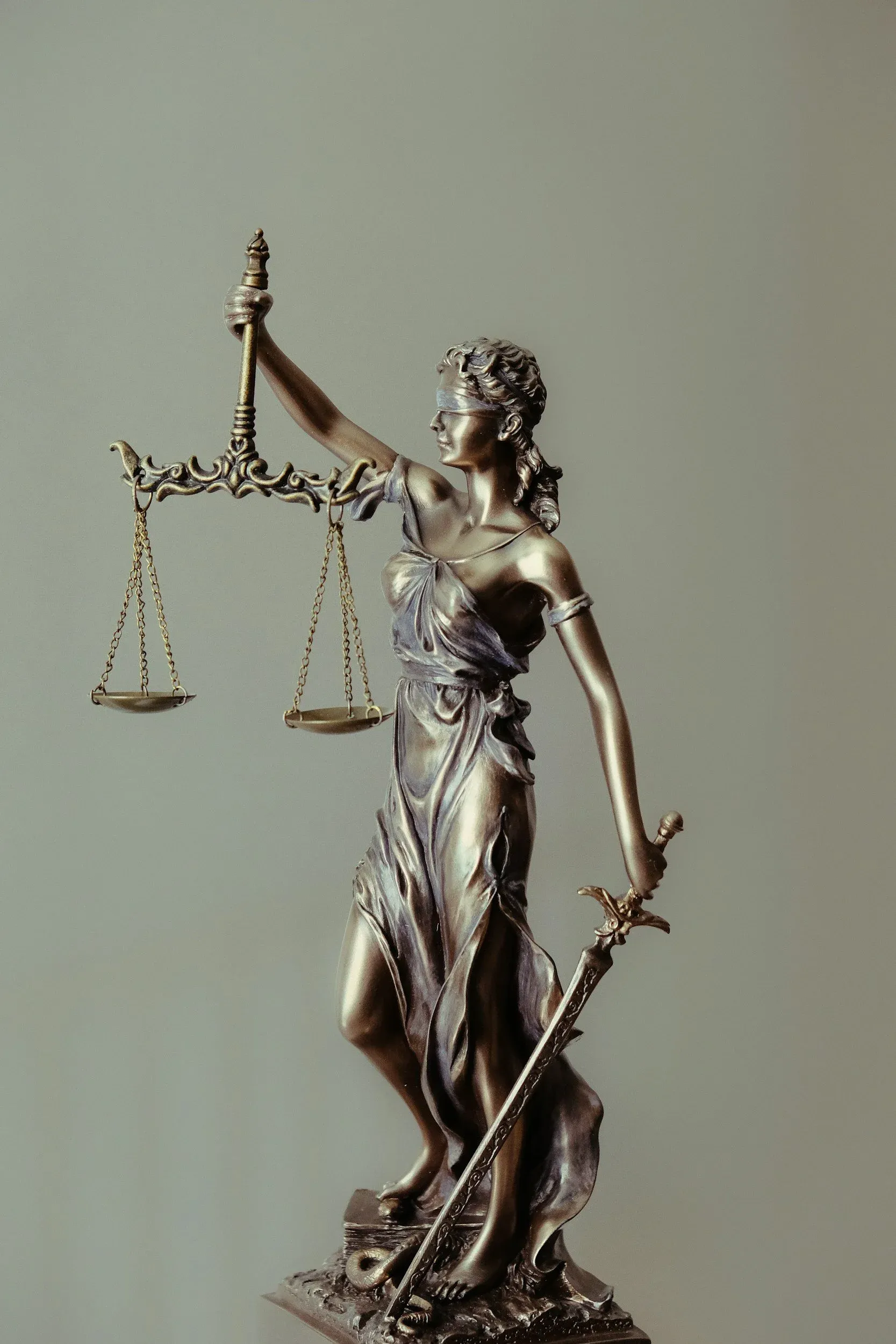 Bronze statue of Lady Justice holding scales in her left hand and a sword in her right hand. She is blindfolded and wearing a flowing gown.