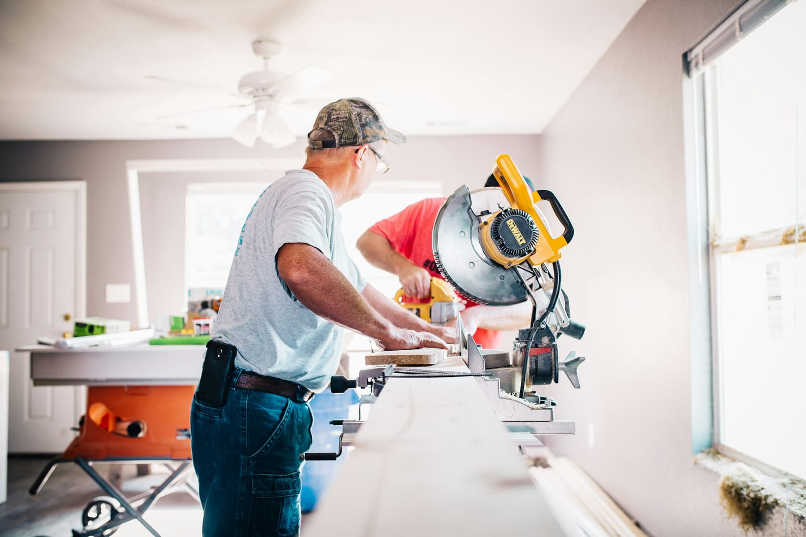 Two tradesmen cutting trim on a miter saw inside a home under renovation