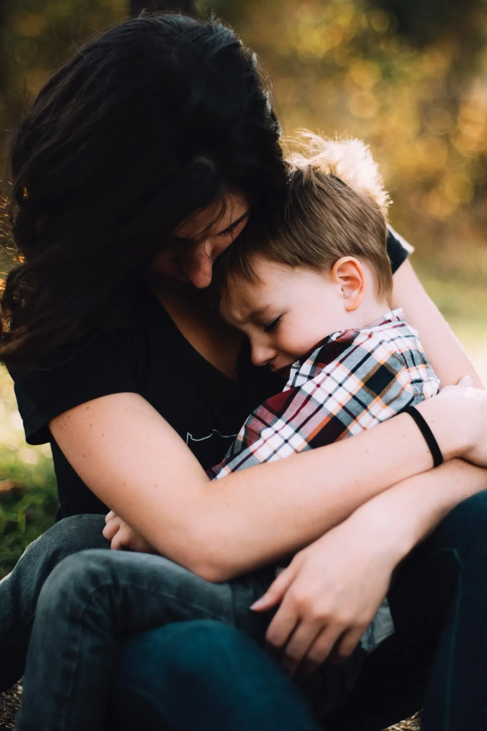 A woman embracing a young child in a plaid shirt outdoors.