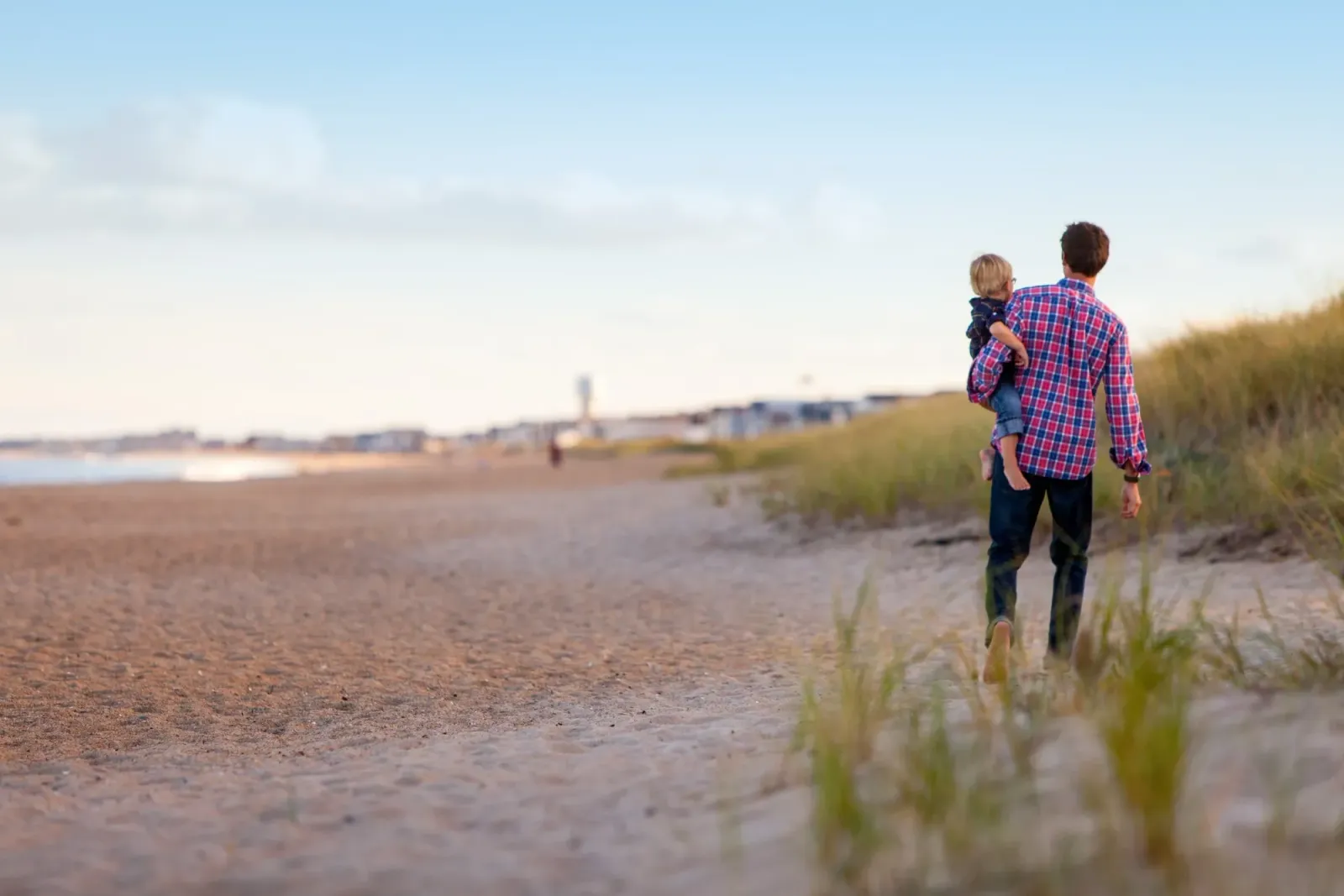 An adult carrying a child along a beach.