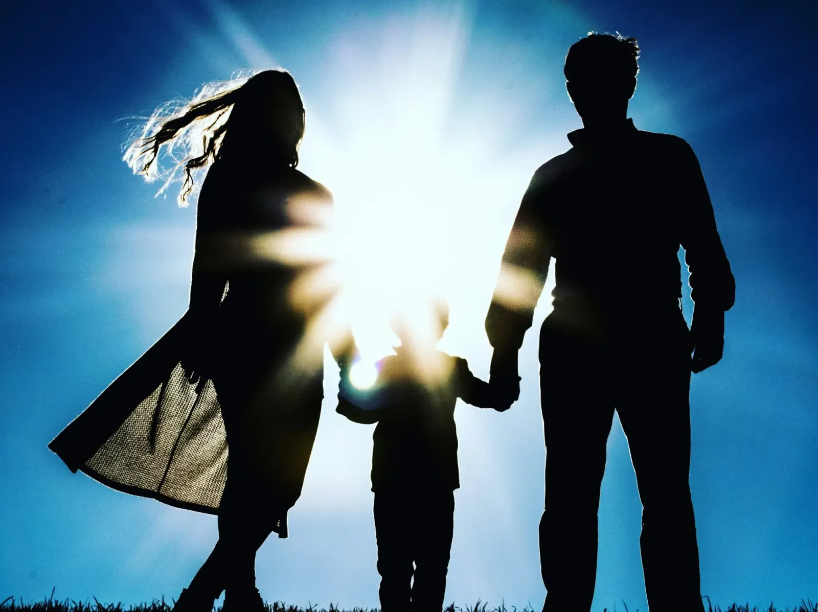 A child holding hands with two adults in sunlight.