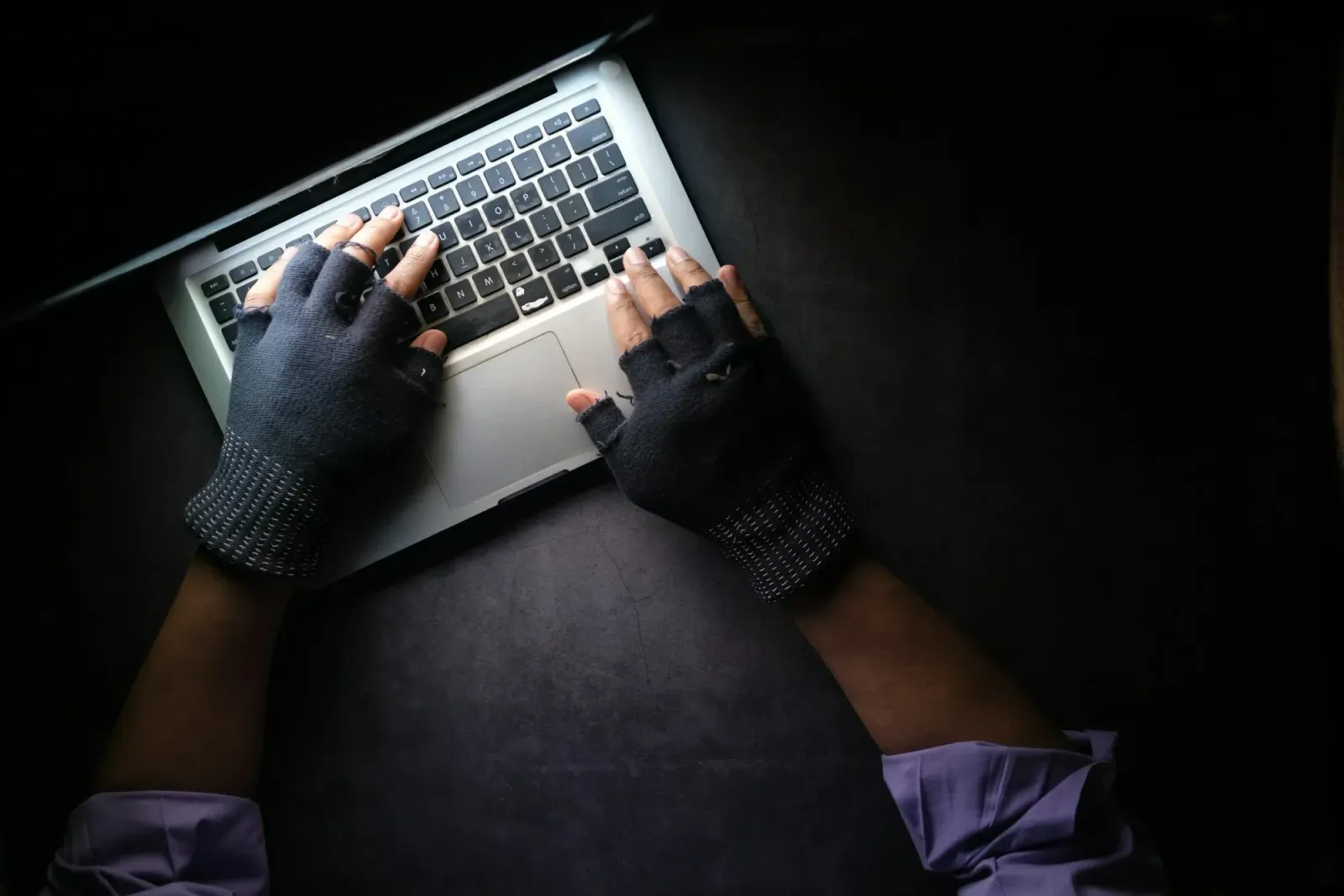 Hands in fingerless gloves using a laptop.