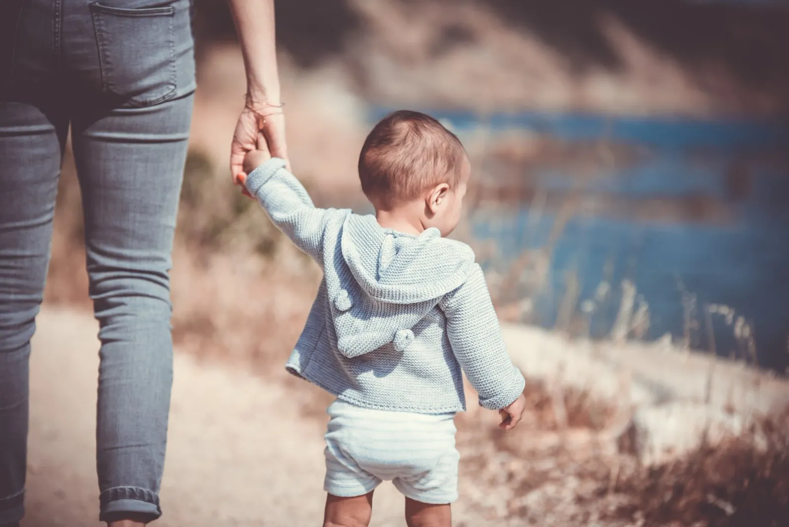 A young child in a knitted sweater beside an adult outdoors.